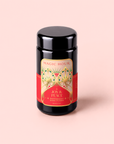 A canister of Peppermint Bark Puerh tea stands upright on a pale pink background, its red and gold label promising the rich aroma and metabolism-boosting benefits of this dark chocolate peppermint blend.