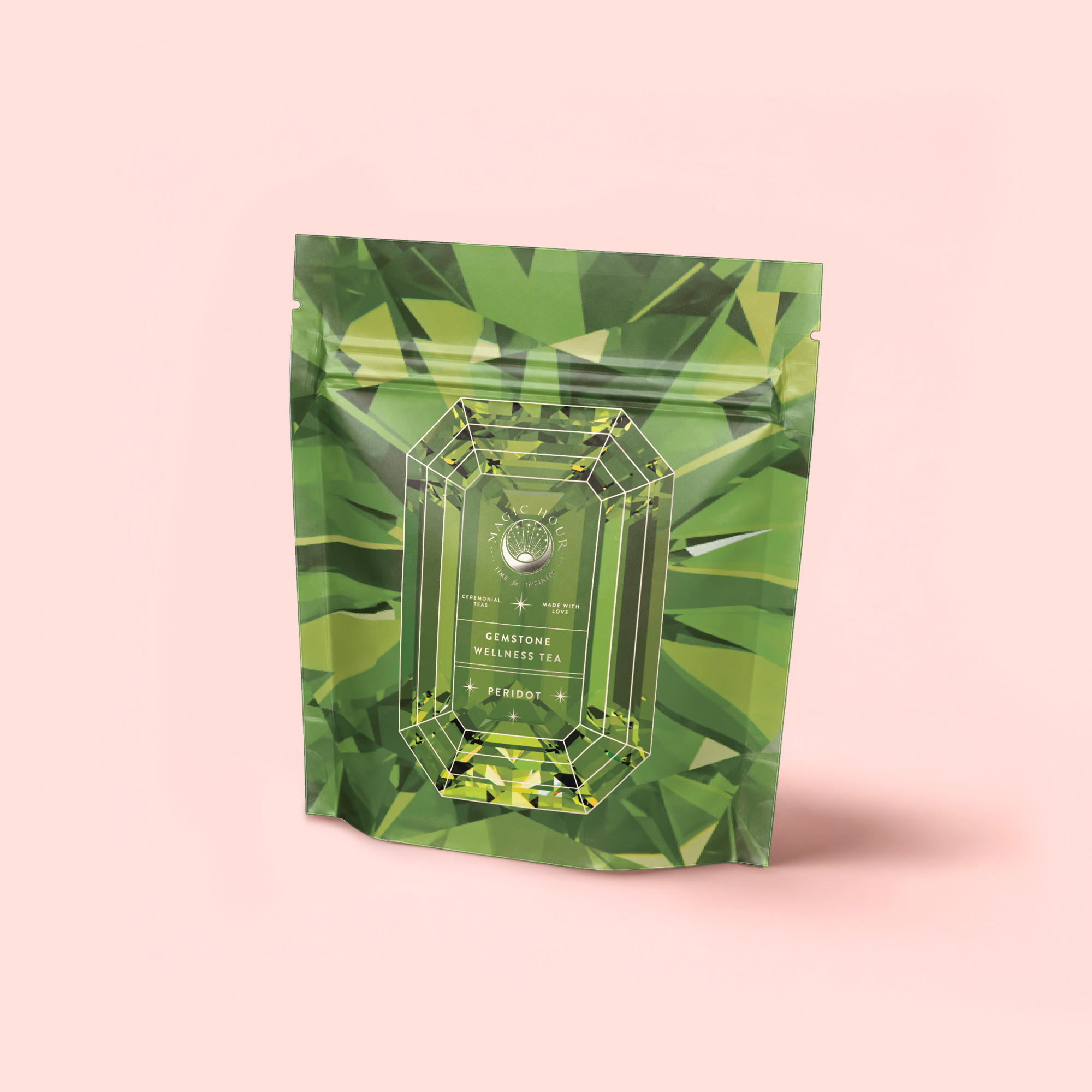 A green, gemstone-patterned pouch labeled "Peridot: Green Guayusa Oolong Mango-Peach Tea" stands upright against a light pink background, featuring a faceted gemstone design and highlighting its refreshing mango-peach flavors.