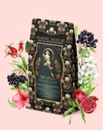 A floral and fruit-inspired tea package labeled "Persephone's Potion: Pomegranate & Jasmine Green Tea" stands surrounded by illustrated flowers, berries, pomegranate, and rose hips on a soft pink background—inviting you to indulge in the enchanting blend of pomegranate and jasmine green tea.