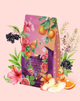 Experience Pink Moment Pixie - Hibiscus Tangerine Dream Herbal Tea in a vibrant package adorned with charming illustrations of hibiscus, tangerines, figs, blackberries, apples, and lush green leaves set against a light pink background—reflecting the lively flavors within. Savor a refreshing cup of this naturally caffeine-free tea, rich in vitamin C and perfect for any time of day.