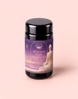 A jar of “Pitta: Caffeine-Free Saffron Tea for Balancing Body, Mind & Emotions” rests on a pale pink background. The label is adorned with calming purple hues, a crescent moon, and gentle silhouettes, creating an atmosphere of relaxation and peace. This soothing floral blend is thoughtfully crafted to help restore balance and tranquility as you unwind in the evening.