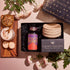 The Pumpkin Lovers Tea & Accessory Gift Set includes a tea canister, a ceramic ceremonial tea bowl, and an "Exquisite Star Sips" package. Alongside it, you'll find a frothy pumpkin spice tea accompanied by cinnamon sticks, cookies, and white flowers beautifully displayed on a wooden board.