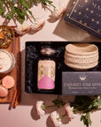 The Pumpkin Lovers Tea & Accessory Gift Set includes a jar labeled "Magic Hour," a box of "Exquisite Star Sips," a luxurious ceremonial tea bowl, and a cup of pumpkin spice tea. It comes paired with macarons and cinnamon sticks, all beautifully arranged on a wooden tray with decorative flowers elegantly surrounding these delightful items.