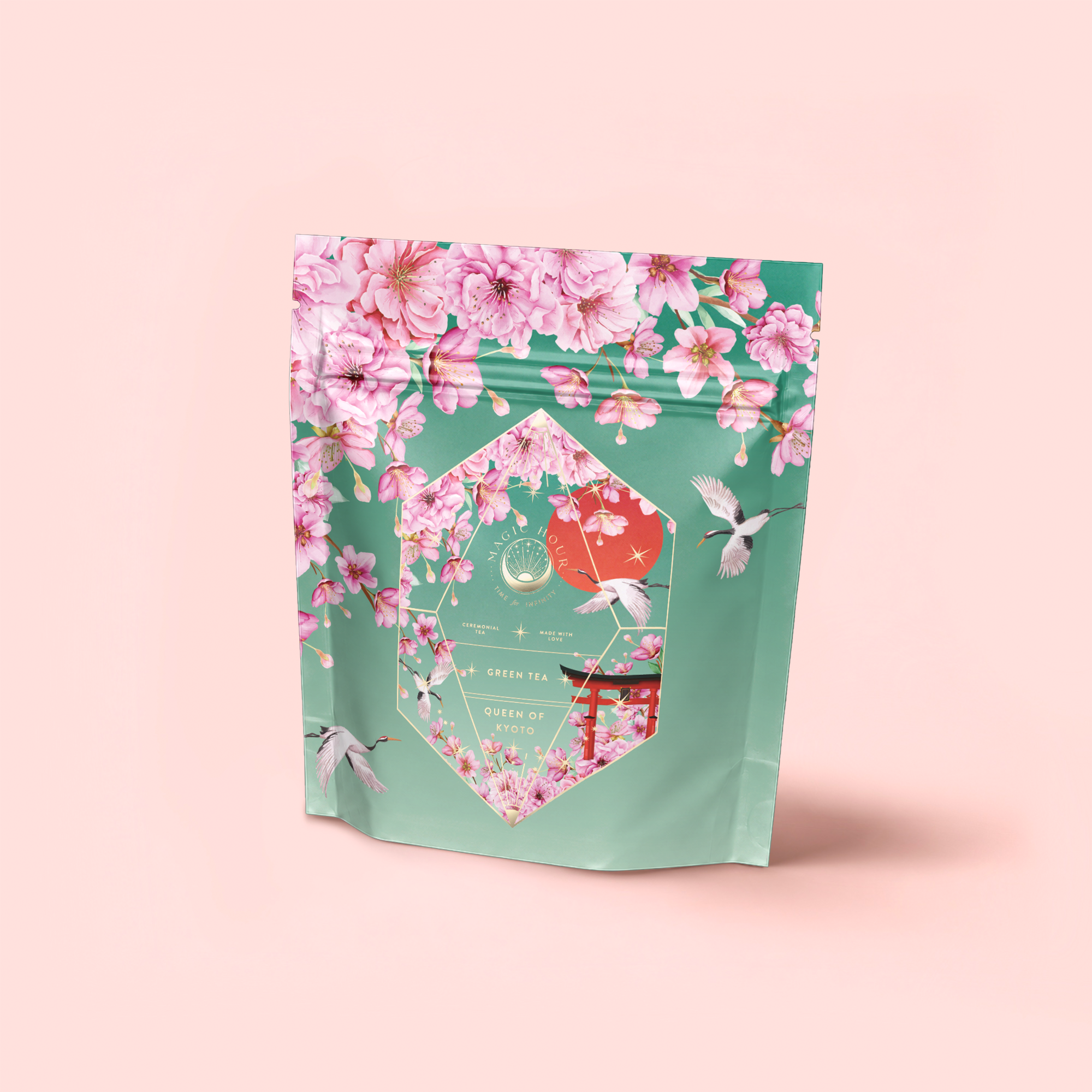 A pastel green tea pouch with pink cherry blossoms, white flying birds, and gold accents evokes the Japanese Cherry Blossom Festival. The label reads “Queen of Kyoto” and hints at delicate Sencha Green Tea within.