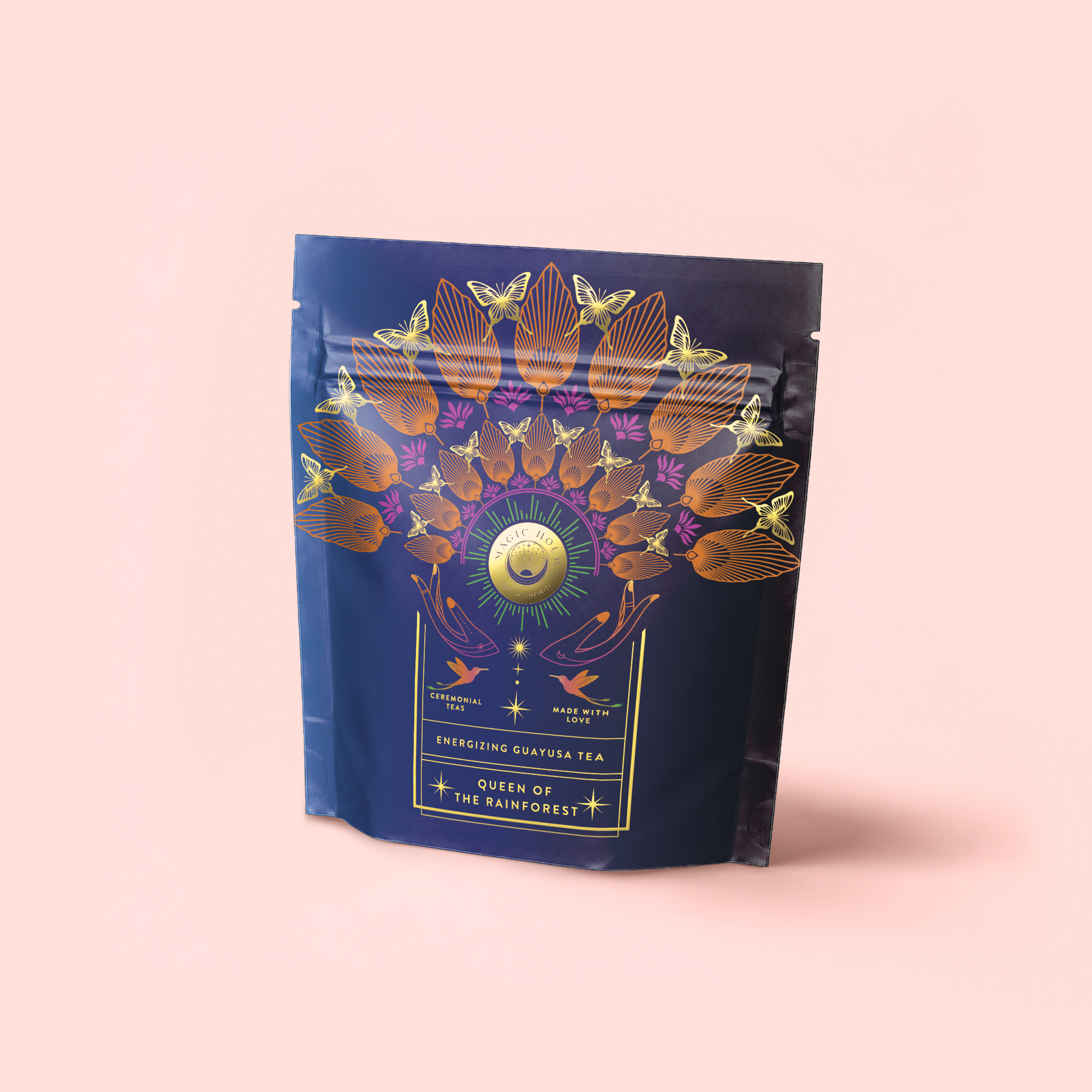 A navy blue tea pouch with vibrant floral and bird designs, gold accents, and a pale pink label that reads "Queen of the Rainforest: Cacao-Berry Tea," featuring an energizing rainforest blend.