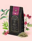 The Raspberry Earl White Tea package in black and gold is shown with fresh raspberries, antioxidant-rich white tea leaves, raspberry leaves, and white camellia flowers on a soft pink background.