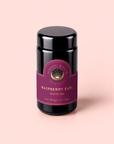 A dark jar with a purple label reading “Raspberry Earl White Tea, Net Weight 1oz (28g)”—a delightful blend infused with the subtle aroma of bergamot and packed with antioxidants—sits on a light pink background.