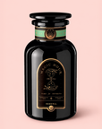 A black glass tea jar labeled “Renewal: Peach-Goji-Rose Oolong Tea” with gold and teal accents, adorned with celestial graphics and a round lid. Set against a light pink background, it evokes the lush notes of Oolong tea infused with hints of peach, creating an enchanting tea experience.