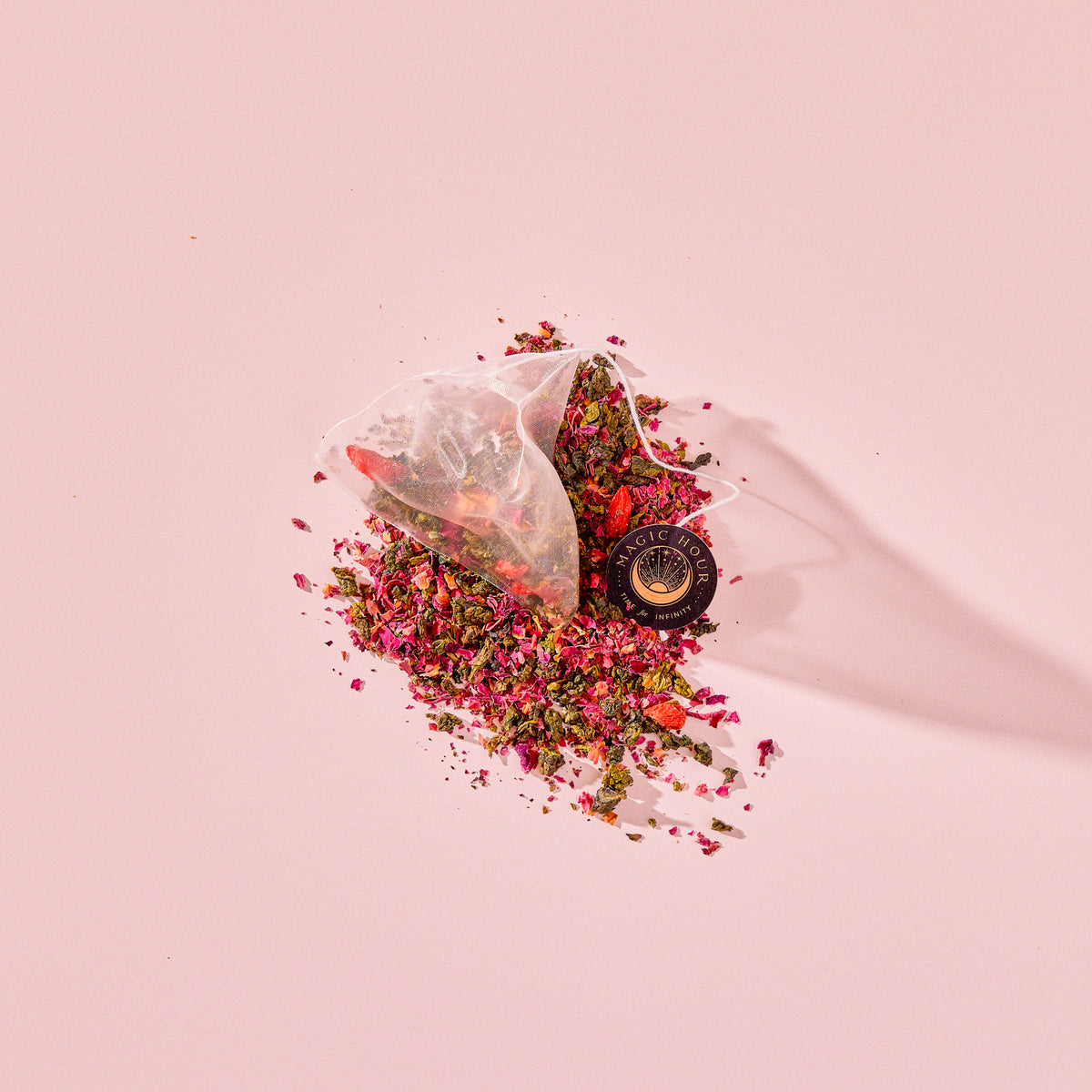 A Tea for Beauty: Renewal: Peach, Goji &amp; Rose Oolong Tea pyramid bag resting on a pile of loose-leaf peach oolong tea, dried rose petals, and goji berries.