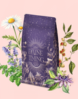 A purple coffee bag labeled "Divine Timing Rest" sits among illustrated chamomile, lavender, passionflower, and coffee plant branches on a pale pink background.