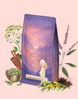 A bag of Restful Evening Chai: Dosha Balancing Saffron Spice Tea, a soothing caffeine-free herbal chai blended with powerful herbs, cinnamon sticks, cardamom pods, and tea leaves, is artfully arranged on a pale pink background. The packaging features a sunset and silhouette design, highlighting its purpose as a Dosha balancing tea for daily wellness.