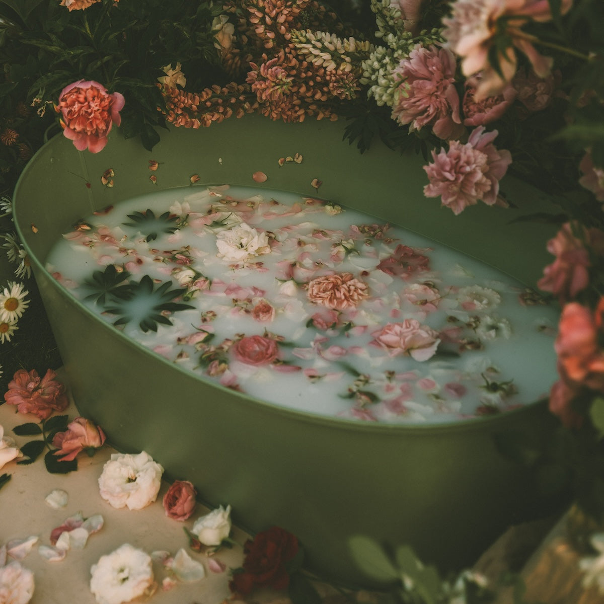 Transform your self-care ritual with the Ceremonial Bath Soaks - Luxe Refill Pouch; green bathtub brimming with milky water and floating blooms creates a serene, cosmic connection to tranquility. Lush flowers cascade over the edges, crafting a peaceful, vibrant oasis.