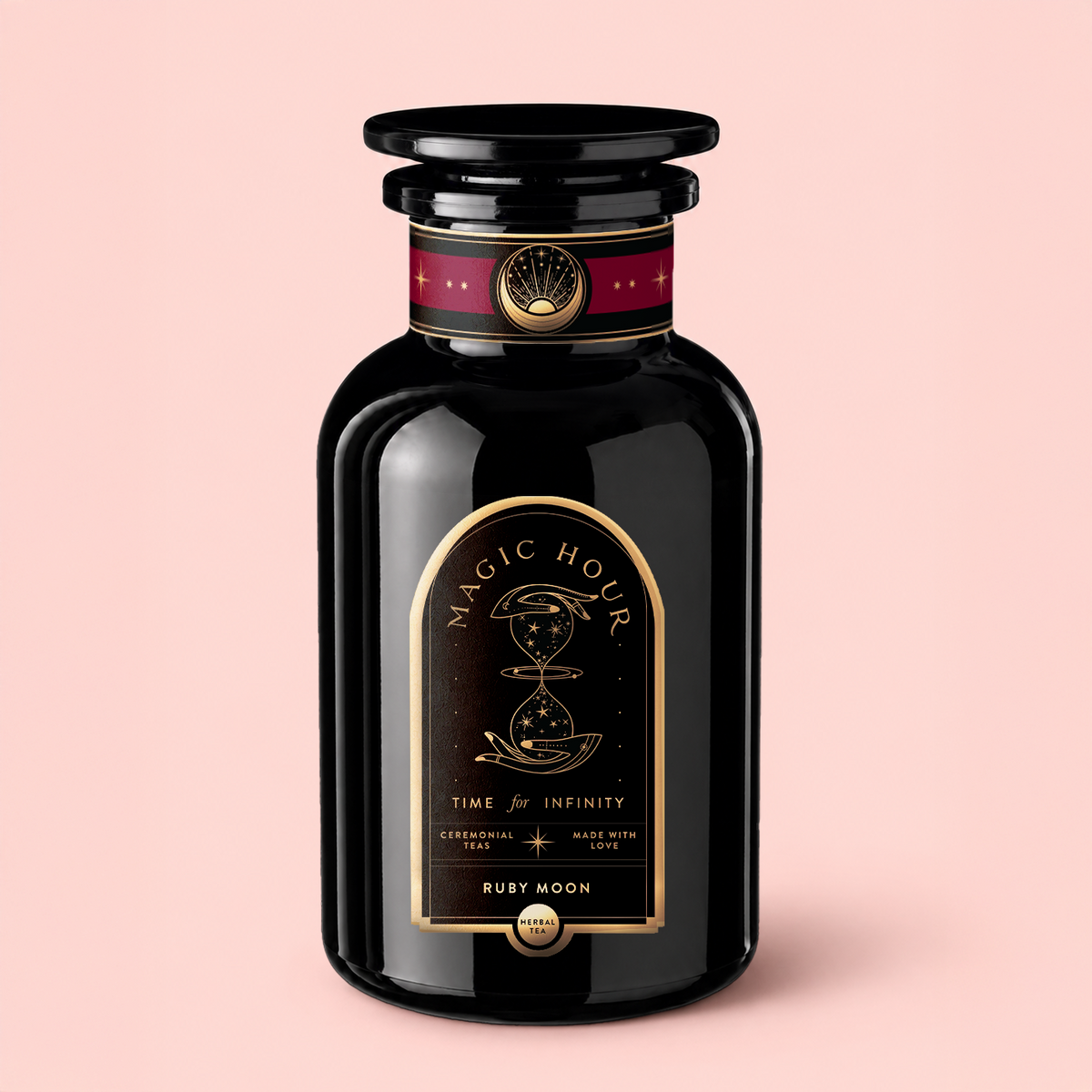 A black apothecary-style jar labeled “Magic Hour Ruby Moon™ : Hibiscus Elderberry Tea” with gold celestial designs stands on a light pink background. The label features “Time for Infinity” and notes that it is a “Ceremonial tea made with love.” This exquisite jar contains a healing herbal blend—a luxurious, caffeine-free hibiscus elderberry tea that’s as enchanting as its celestial motif.
