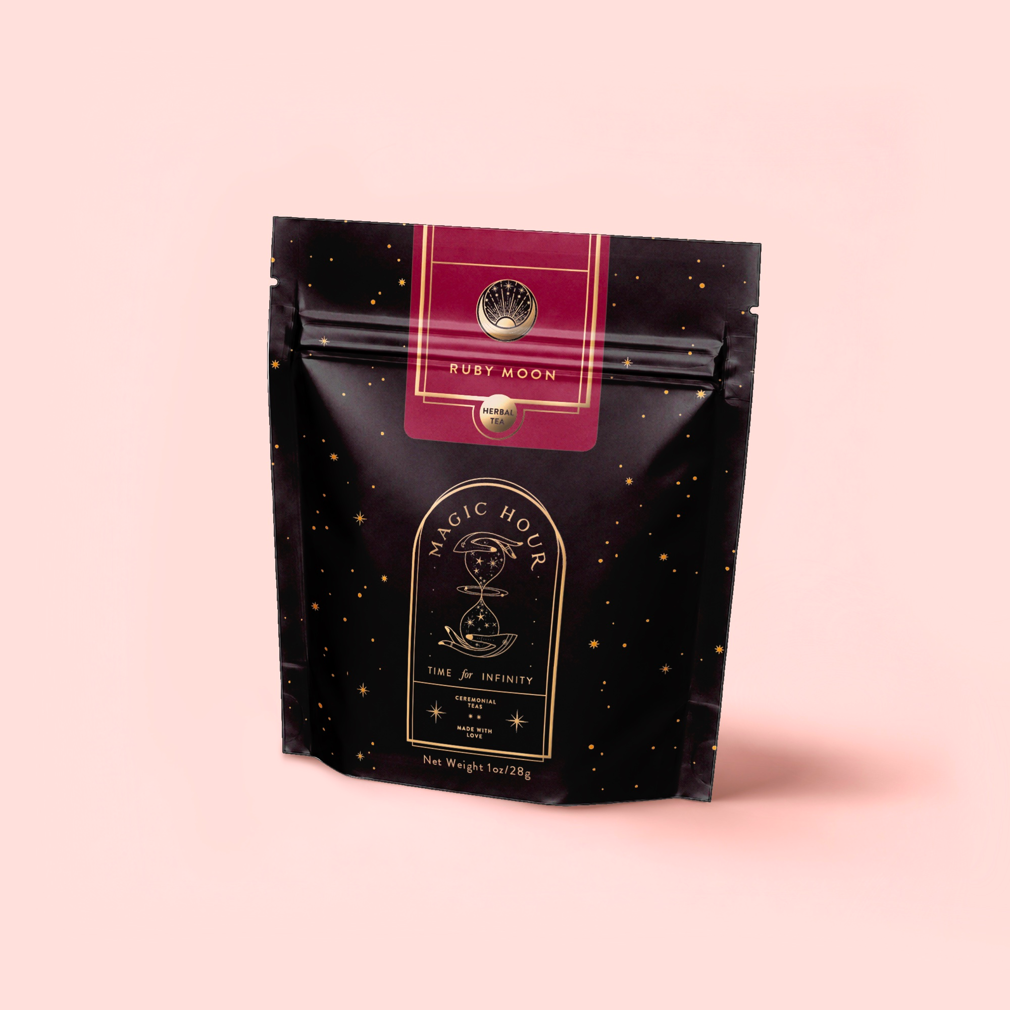 A black and gold resealable pouch labeled "Magic Hour" with a celestial design holds caffeine-free Ruby Moon™: Hibiscus Elderberry Tea, rich in vitamin C, set against a light pink background.