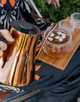 A copper tea kettle pouring hot water into a glass teapot filled with S'mores Herbal Dessert Loose Leaf Wellness Tea on a Wooden tea tray.
