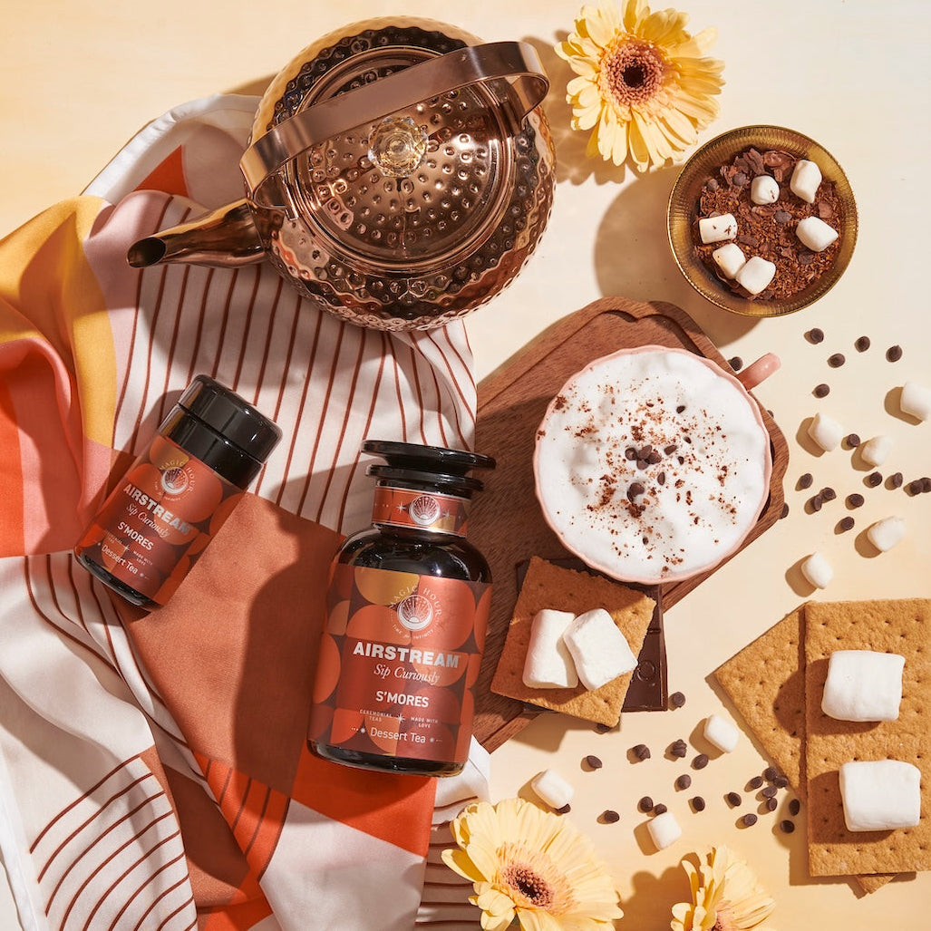 S'mores Loose Leaf Dessert Herbal Tea Top Down on a Table with Graham Crackers, Marshmallows, Chocolate, Loose Leaf tea, and a silk scarf as well as a copper tea pot