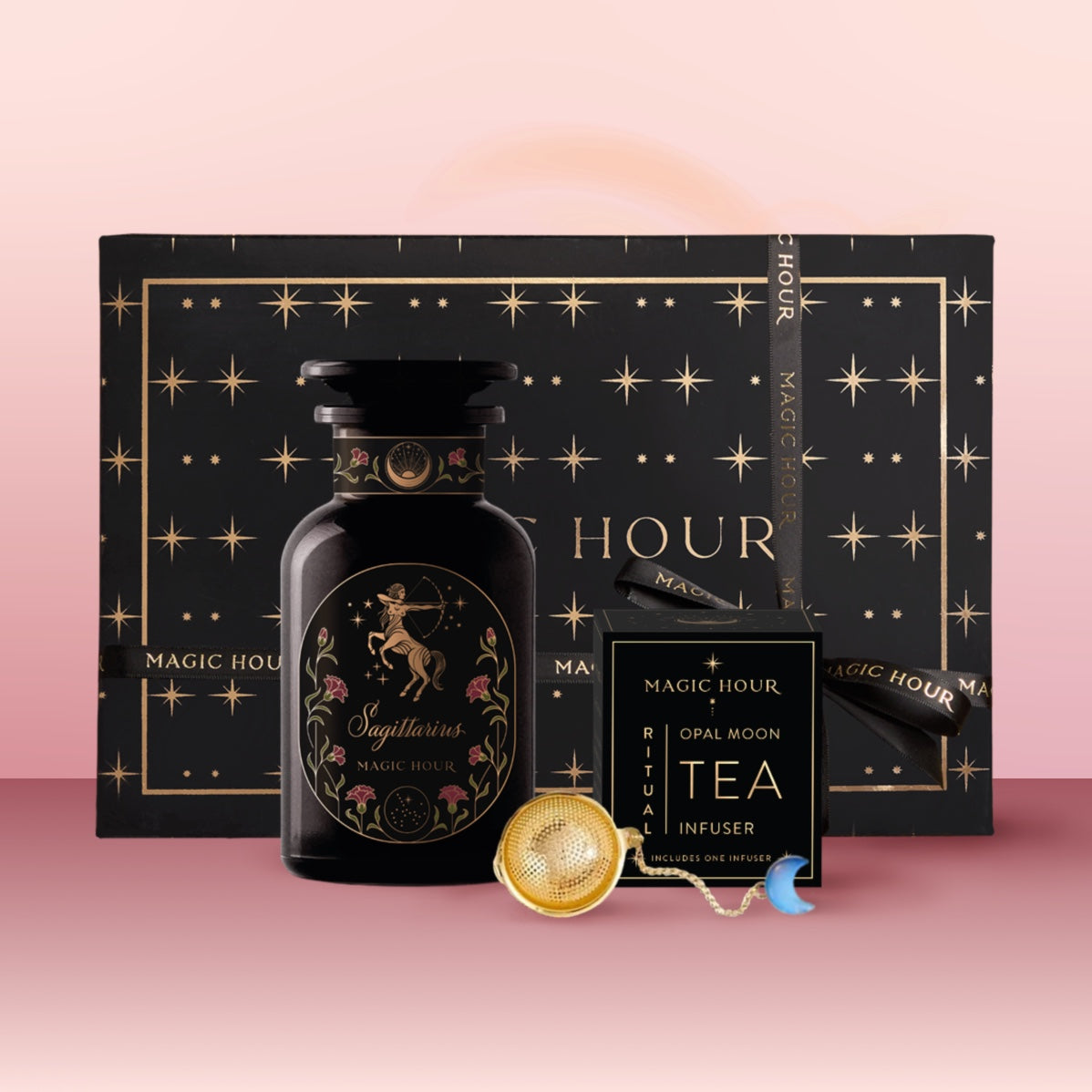 The Sagittarius Astrology Tea Gift Set includes a black “Magic Hour” gift box with gold stars, a black jar with a Sagittarius centaur, a tea infuser, and an “Opal Moon Ritual Tea Infuser,” all beautifully arranged on a pink background.