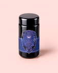 A dark jar with a blue geometric label reading “Sapphire: Apple-Plum-Spice White Tea for Self-Expression” is set against a light pink background, inviting you to experience the soothing elegance of this premium organic blend designed to inspire self-expression.