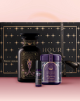 The Saturn Bath & Beauty Box features a sacred beauty box, a large black jar with mystical design, a small roll-on, and a purple container, all arranged on a pink surface to inspire grounding energy.