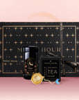 The Scorpio Astrology Tea Gift Set, with star designs in black and gold, features Astrology Tea in a tin, an Opalite Moon Tea Strainer, and a tea packet, all arranged before a decorative box on a pink background.