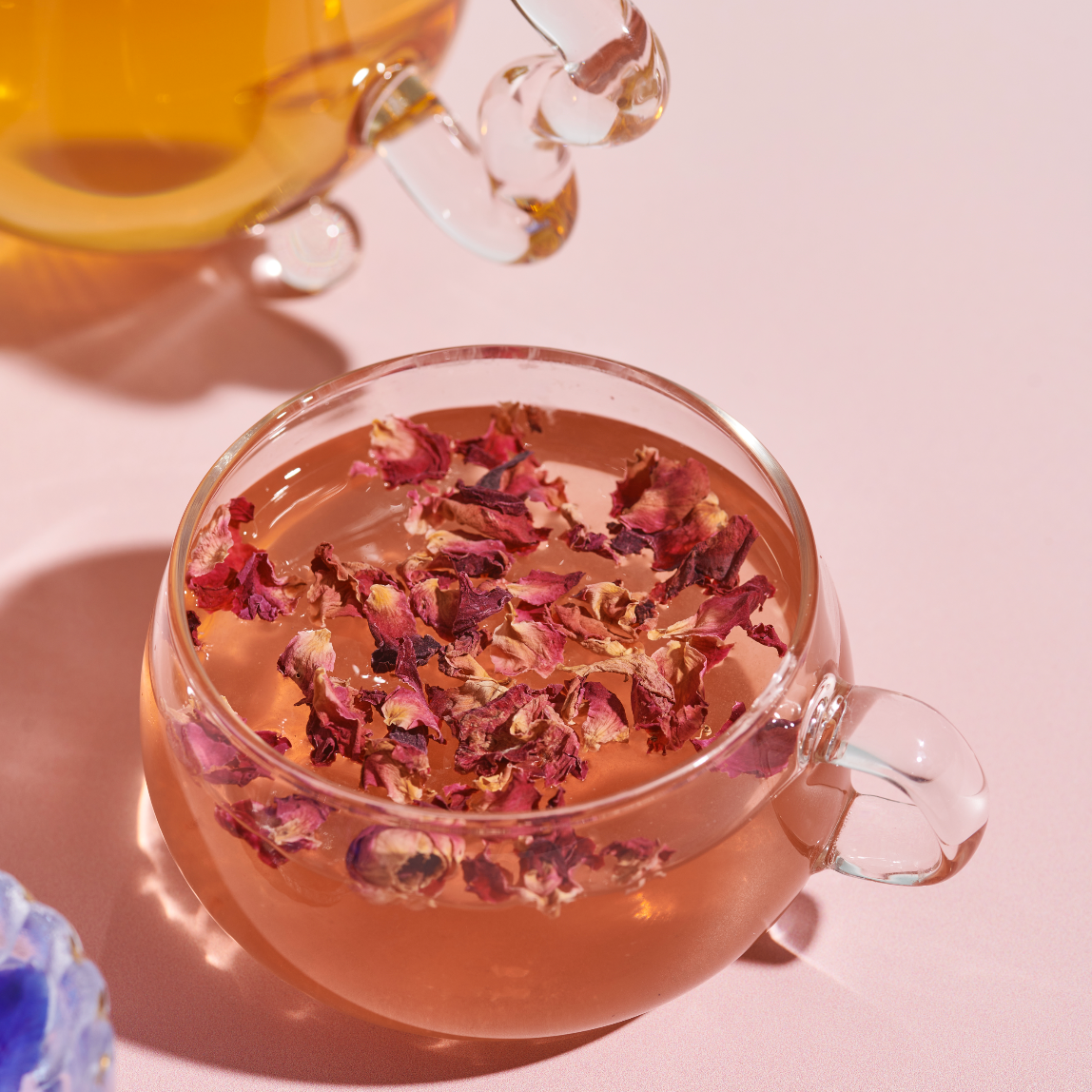 Clear glass mug with dried flowers floating in a pinkish liquid on a light pink background