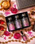A She Rises Goddess Moonlit Bloom Apothecary Gift Box containing three apothecary jars of moonlight white tea, a spray bottle, and a gold teapot, surrounded by pink flowers, a tray with two cups of tea, and beaded garlands.