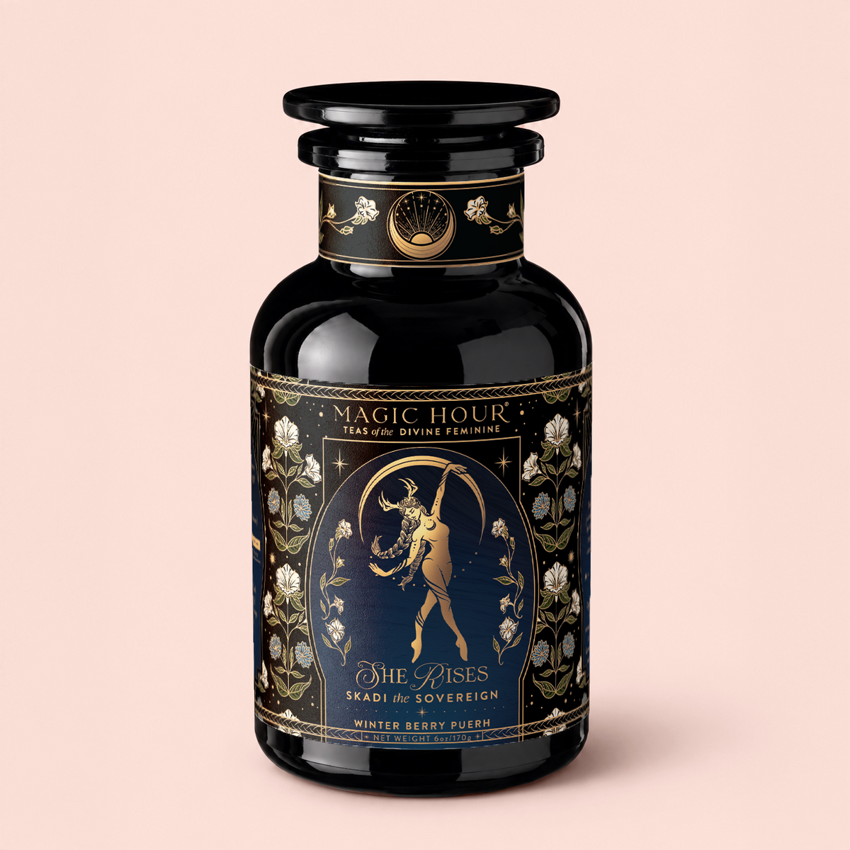 A black and gold canister labeled “Skadi The Sovereign: Winter Berry Puerh” displays an illustration of a woman with a bow, surrounded by floral designs, and text reading “The Rises.” With its berry-infused pu’erh blend, this tea is perfect for enjoying on chilly evenings and celebrates the resilience of winter. The background features a soft light pink hue.