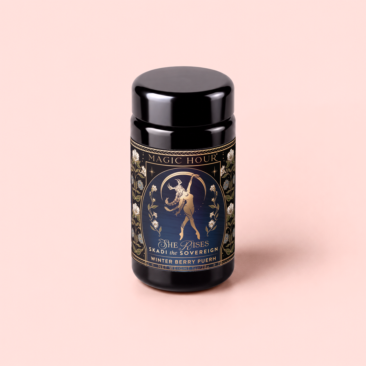 A black jar labeled “MAGIC HOUR” with an intricate design depicts a woman holding a wolf and a sword. The label reads “She Rises: Skadi The Sovereign: Winter Berry Puerh.” This striking berry-infused tea embodies the spirit of winter resilience. The jar is set against a light pink background.