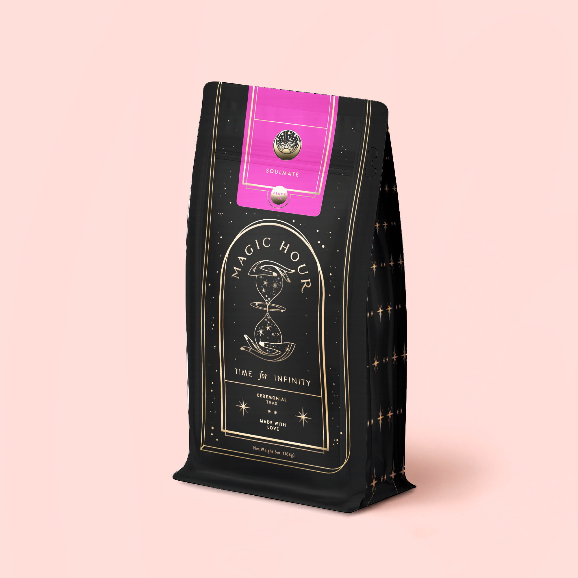 A black and gold tea pouch labeled "Soulmate: Chocolate-Raspberry-Rose Black Tea Refill" with an hourglass illustration and pink seal stands upright on a light pink background, suggesting the enchanting organic blend inside.