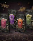 Four black, purple, orange, and green Spellbound Sips Bundle stand-up tea pouches, each with a gold label featuring thematic illustrations like a bat, a cat on a crescent moon, and a witch’s hat.