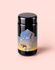 A canister of Sri Lankan Sunrise, featuring a colorful geometric label with nature-inspired illustrations, sits atop a soft pink background. This elegant container holds organic black tea—an ideal choice for savoring as a classic Sri Lankan breakfast brew.