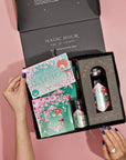 A person opens a Monthly Magic 3-Month Tea Subscription Box, unveiling a selection of Kyoto-themed tea products. The packaging is adorned with cherry blossoms and a teal color scheme. With nails painted blue, they savor the herbal teas, while a ring on one hand glimmers in the light.
