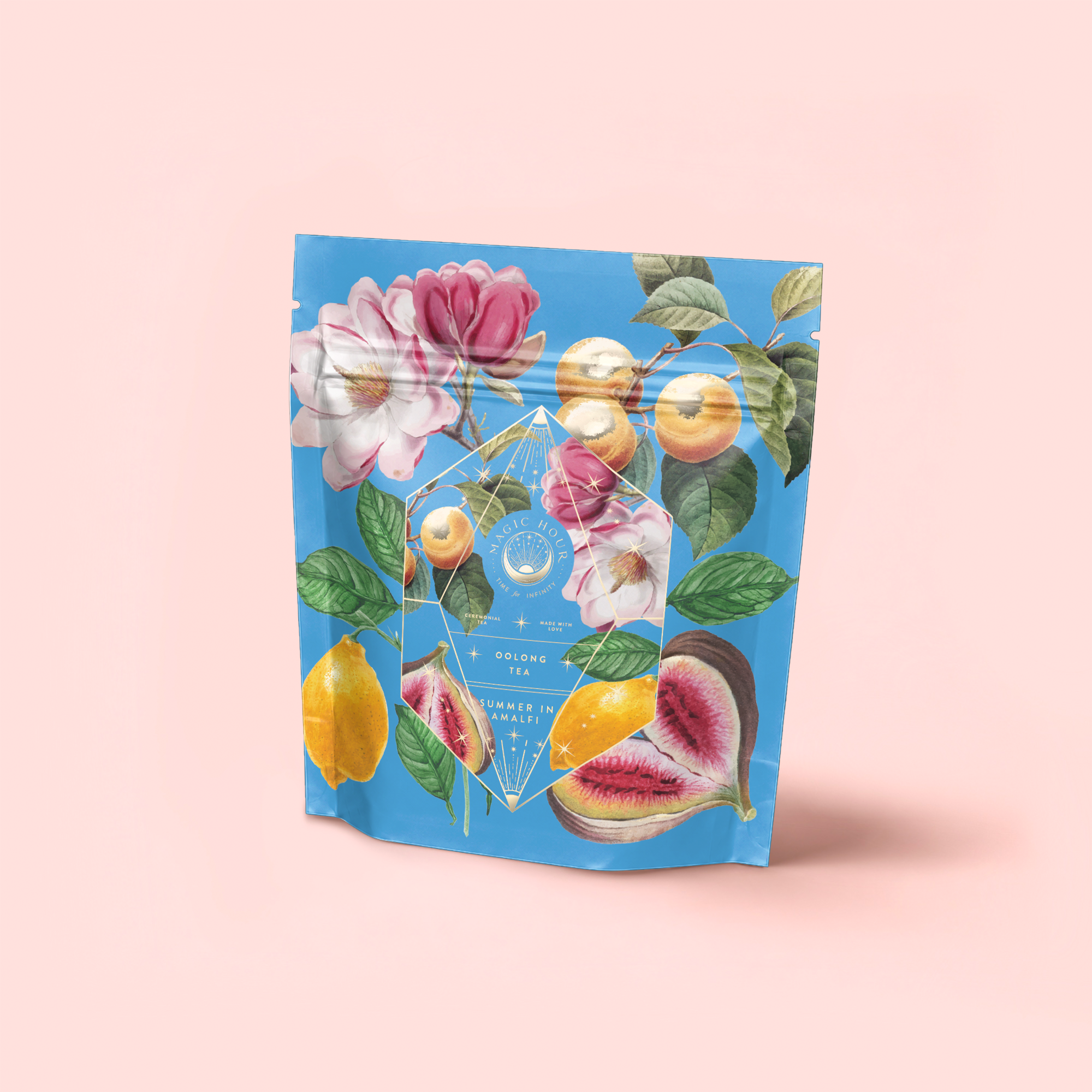 A blue resealable pouch of "Summer in Amalfi" stands upright against a pale pink background, featuring colorful illustrations of flowers, lemons, figs, and cashew fruits that highlight its Mediterranean Tea blend with Lemon Bergamot.