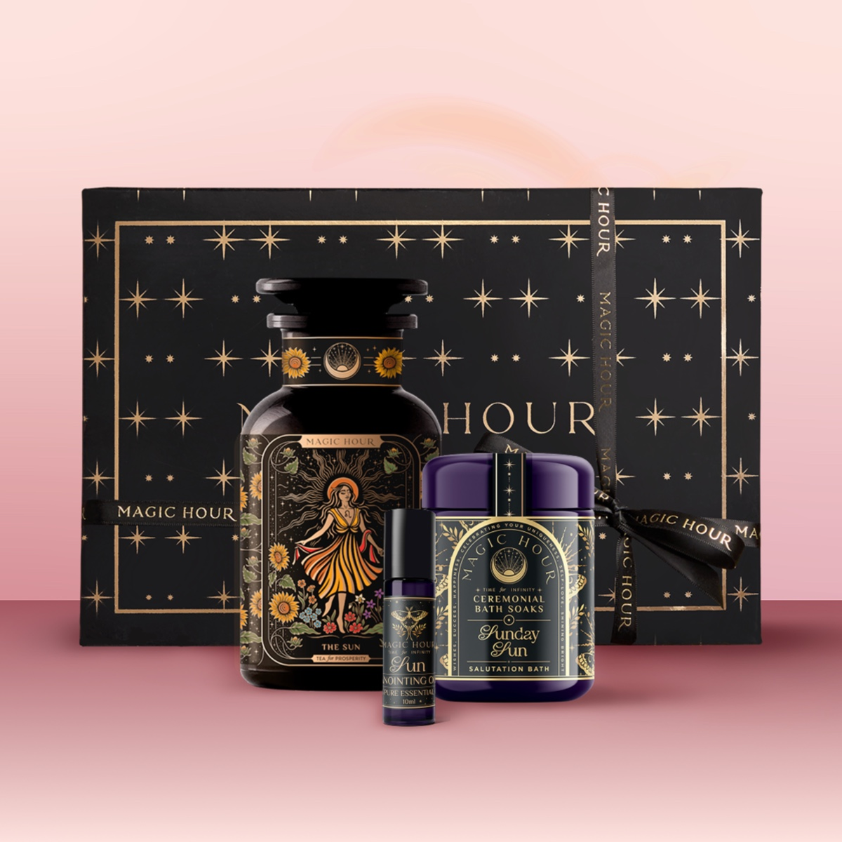 The Sun Bath & Beauty Box is a luxury gift set in a black box with gold stars, featuring a bottle, jar, and lip balm—each decorated with celestial sun-themed labels on pink, infused with adaptogenic botanicals.