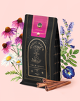 A Symbeeosis: Chamomile Elderberry Green Tea Refill Pouch stands amid illustrated chamomile, elderberry, green tea leaves, and cinnamon sticks—a vibrant wellness tea blend set against a pale pink background.