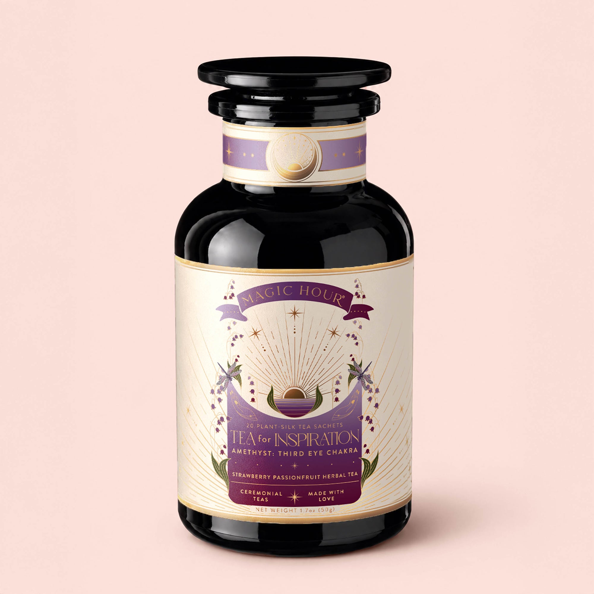A black glass jar labeled "Tea for Inspiration: Amethyst: Strawberry Passion Fruit Herbal Tea Blend" with a purple and gold design adorned with crystals and celestial symbols, set against a soft pink background. This organic herbal tea blend invites moments of spiritual clarity with every sip.