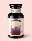 A black glass jar labeled "Tea for Inspiration: Amethyst: Strawberry Passion Fruit Herbal Tea Blend" with a purple and gold design adorned with crystals and celestial symbols, set against a soft pink background. This organic herbal tea blend invites moments of spiritual clarity with every sip.