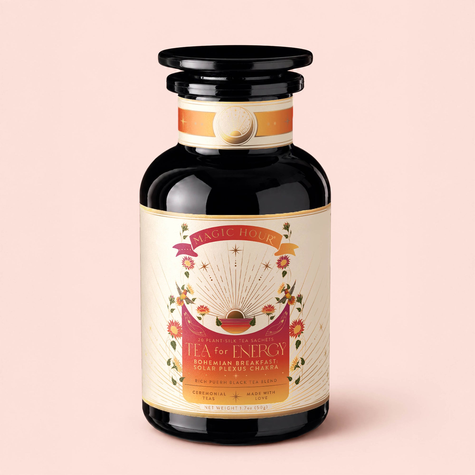 A black glass jar labeled "Tea for Energy: Bohemian Breakfast: Rich Puerh Black Tea Blend" sits on a light pink background. The label is adorned with sun rays, stars, and flowers, evoking a bohemian spirit and highlighting its energizing organic puerh tea blend designed to support energy and digestion.