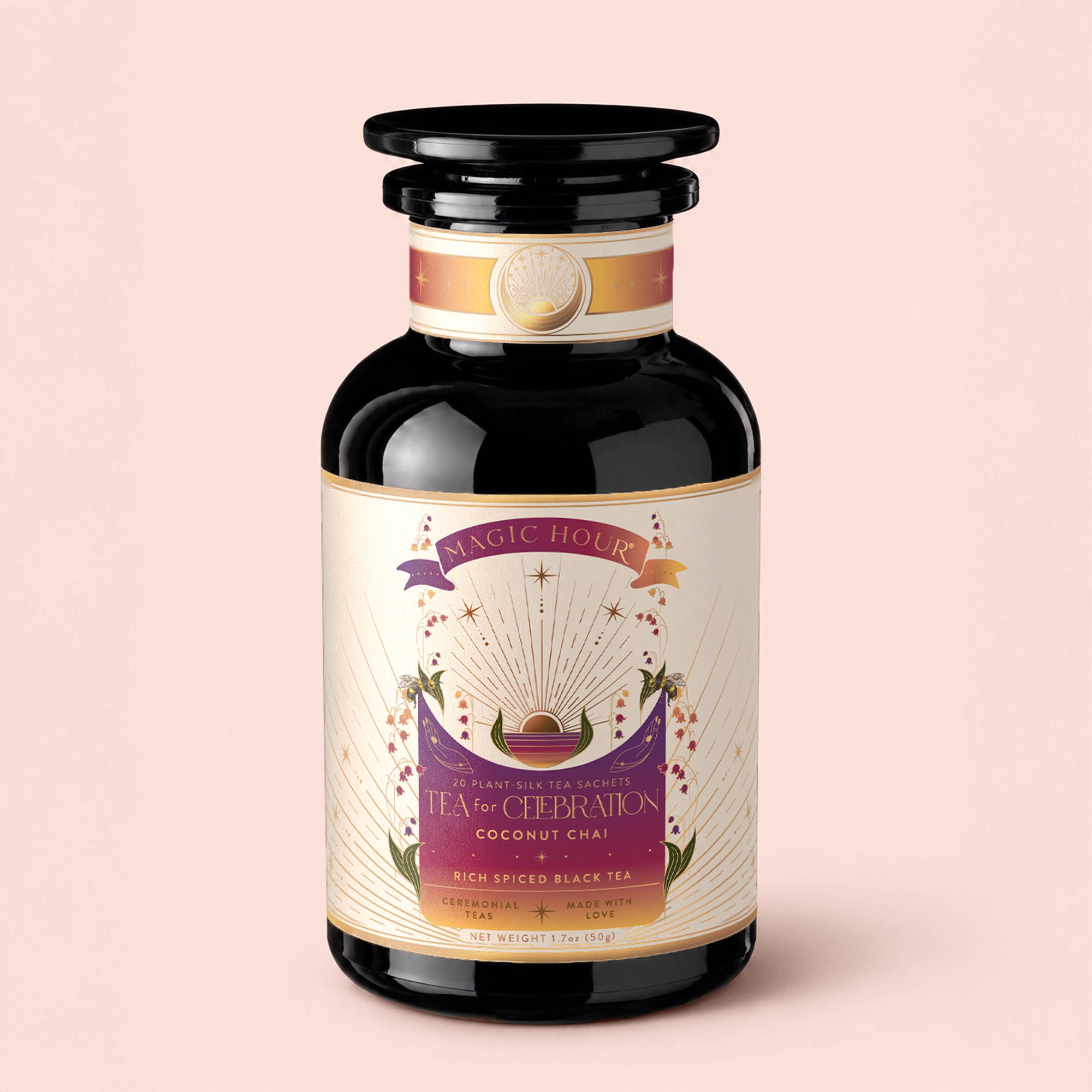 A dark glass jar labeled "Tea for Celebration: Coconut Chai: Rich Spiced Black Tea Blend" features a purple and gold design adorned with stars and radiant rays, evoking crown chakra energy, and is set against a light pink background. The tea inside is a rich spiced black tea blend from Magic Hour.