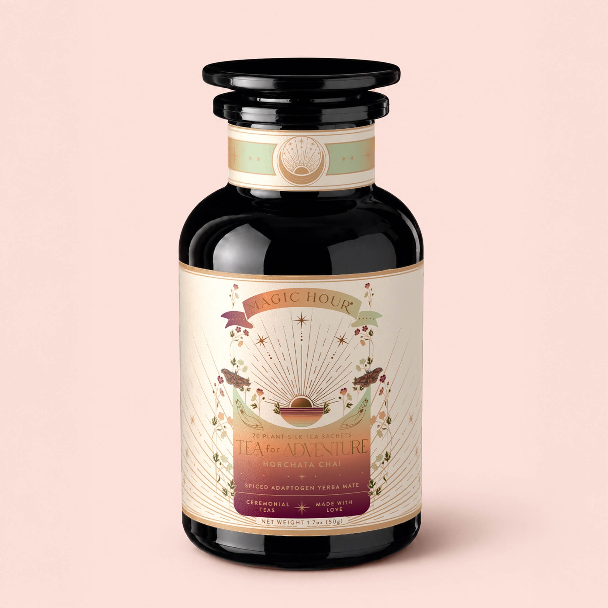A dark glass jar labeled “Tea for Adventure: Horchata Chai: Spiced Yerba Mate” from Magic Hour, adorned with celestial and botanical illustrations—and a touch of Tulum’s spirit—on a cream-colored label, set against a light pink background.