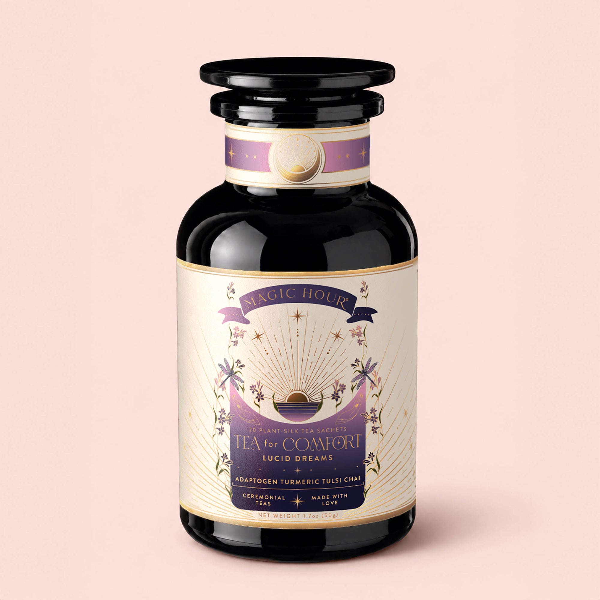 A black glass jar labeled "Tea for Comfort: Lucid Dreams: Turmeric-Tulsi Chai Tea," adorned with gold and purple accents, sun and star illustrations, and a decorative lid, set against a light pink background. This beautifully designed jar contains a caffeine-free herbal tea blend crafted to support restful sleep and encourage soothing dreams.