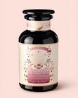 A black glass jar labeled "Tea for the Heart: Pink Tourmaline: Dragonfruit & Hibiscus White Tea" by Magic Hour, adorned with pink, gold, and white designs featuring a sunburst, floral accents, and a heart. The label highlights that it’s a handcrafted heart chakra tea blended with delicate pink white tea and nourishing adaptogenic herbs.