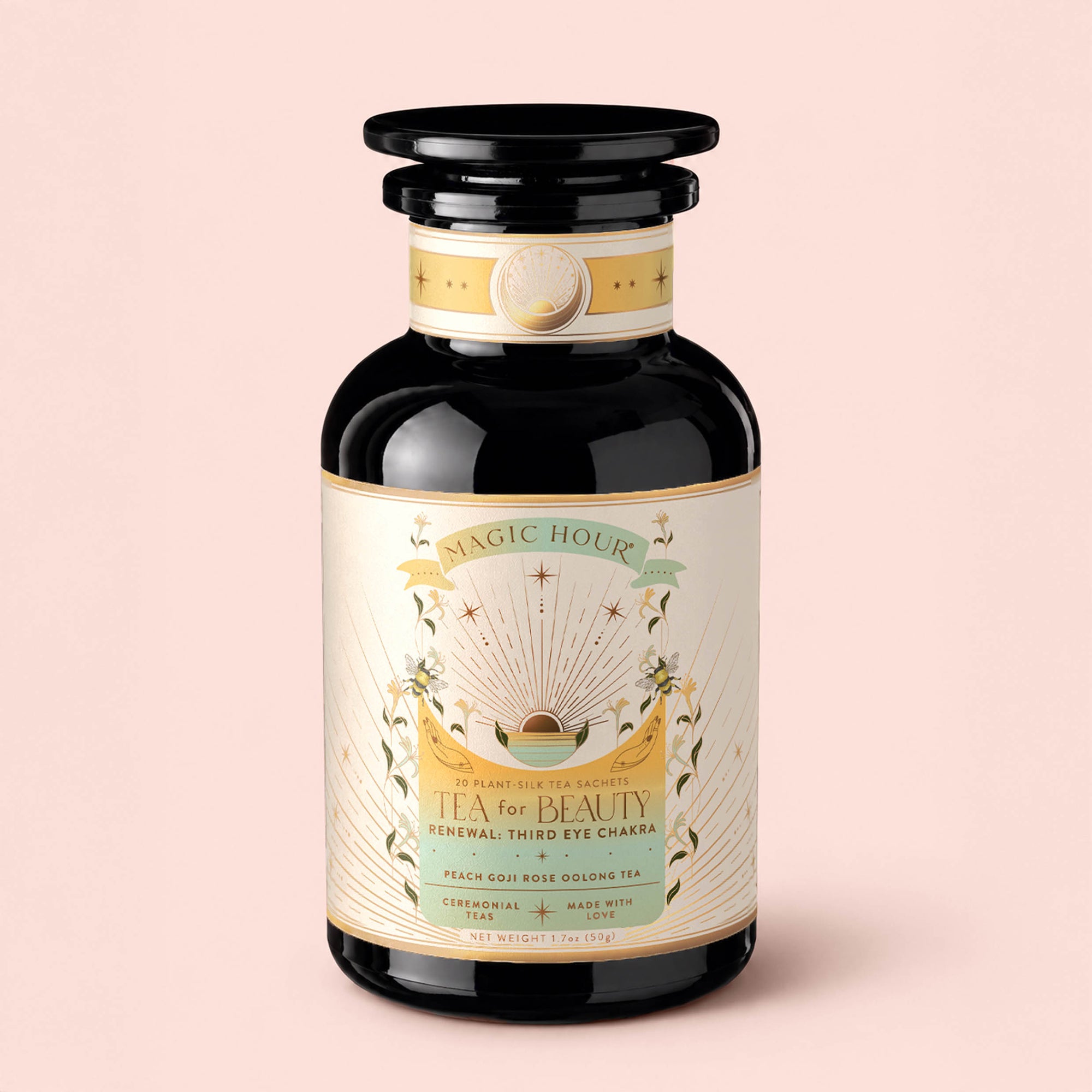 A dark glass jar labeled "Tea for Beauty: Renewal: Peach, Goji &amp; Rose Oolong Tea," adorned with gold and pastel designs featuring celestial and floral elements against a light pink background. This enchanting blend shines with notes of peach, goji, and rose oolong tea, capturing elegance and renewal in every cup.