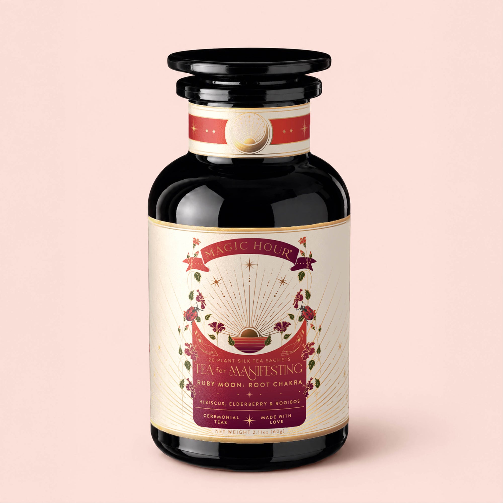 A glass jar labeled "Tea for Manifesting: Ruby Moon: Hibiscus, Elderberry &amp; Passionfruit Herbal Tea" features enchanting illustrations of plants, glowing rays, and a crescent moon set against a pink background. The design exudes a sense of harmony and balance, capturing the essence of manifestation from root to crown chakra.