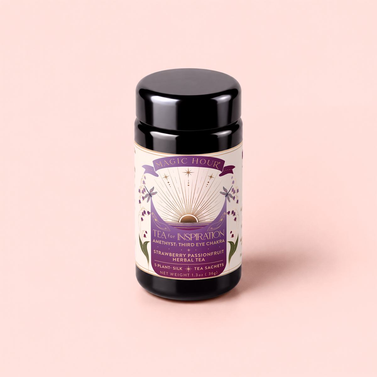 A black tea canister labeled “Tea for Inspiration: Amethyst: Strawberry Passion Fruit Herbal Tea Blend” with organic herbal tea—strawberry passion fruit flavor—featuring a purple and gold design reminiscent of amethyst, set against a pale pink background.