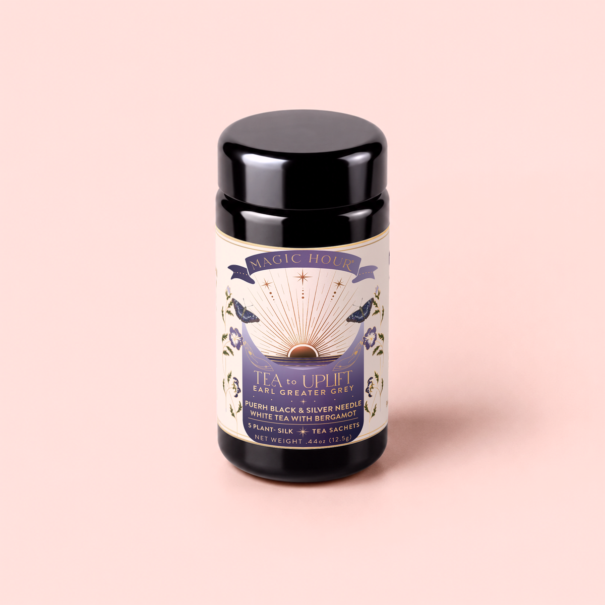 A canister of “Tea to Uplift: Earl Greater Grey—Black & White Tea with Bergamot” rests on a pale pink background, its label adorned with gold and lavender accents and botanical illustrations. The packaging highlights the bright, invigorating blend of organic black and white tea infused with bergamot, reminiscent of a refined classic Earl Grey.