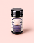 A canister of “Tea to Uplift: Earl Greater Grey—Black & White Tea with Bergamot” rests on a pale pink background, its label adorned with gold and lavender accents and botanical illustrations. The packaging highlights the bright, invigorating blend of organic black and white tea infused with bergamot, reminiscent of a refined classic Earl Grey.