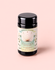 A pastel-designed black tea canister labeled “Tea for Calm: Mantra Mint: Mint With Rose & Vanilla Herbal Tea” features green leaves, roses, and a radiating sunburst on a soft pink background—perfect for storing your favorite mint with rose and vanilla herbal tea blends.