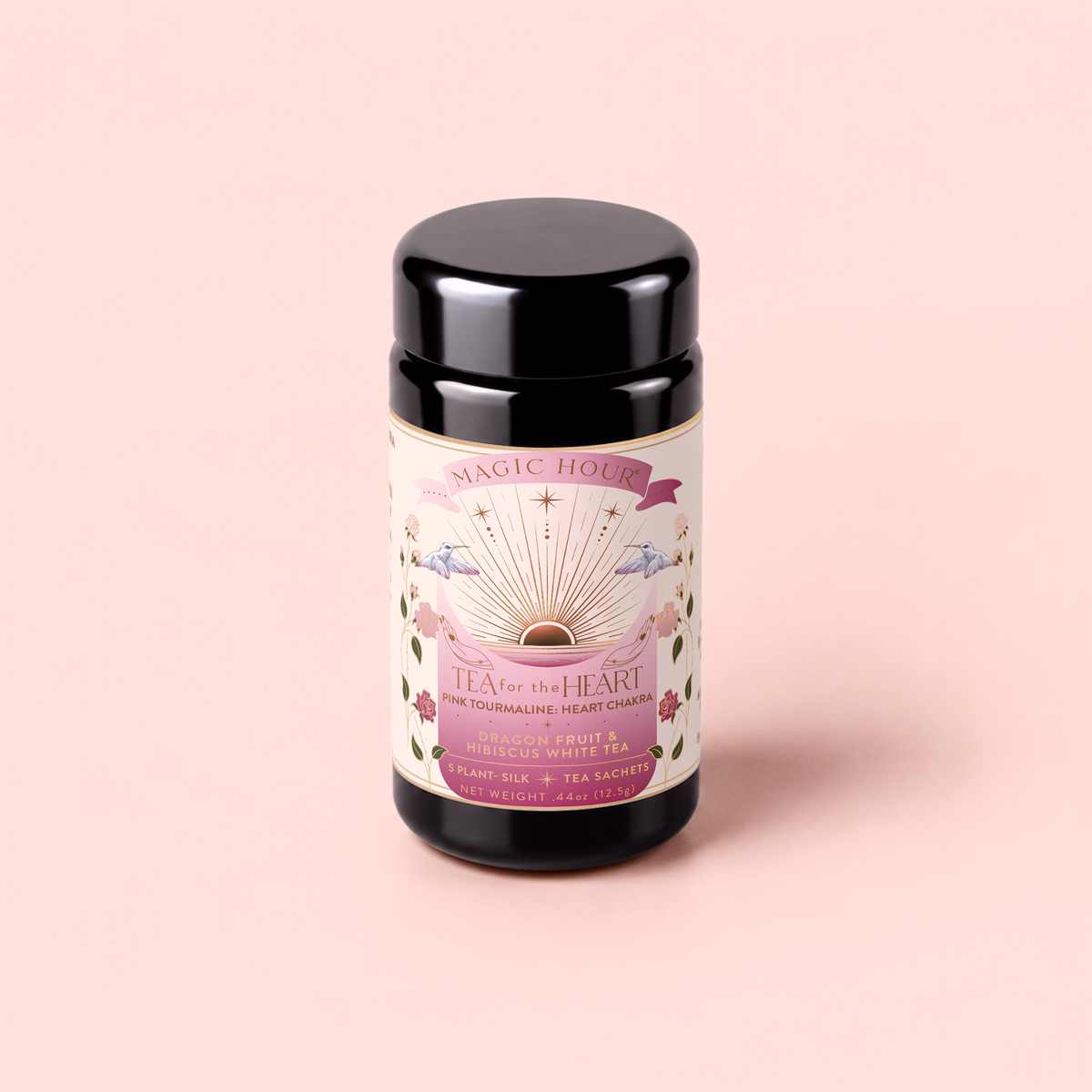A canister of “Tea for the Heart: Pink Tourmaline – Dragonfruit & Hibiscus White Tea” rests on a pale pink background. The label, adorned with floral motifs, two doves, and radiant sun rays, highlights the blend’s hibiscus fruit and adaptogenic herbs. Subtle design elements hint at the delicate allure of dragonfruit and pink white tea.