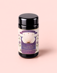 A black tea canister labeled “Tea for Harmony: Queen of Wellness: Women’s Cycle Herbal Blend” with a purple and gold design, featuring an open book, roses, and celestial motifs, sits on a light pink background—perfect for those seeking an organic feminine tea or women’s herbal tea experience.